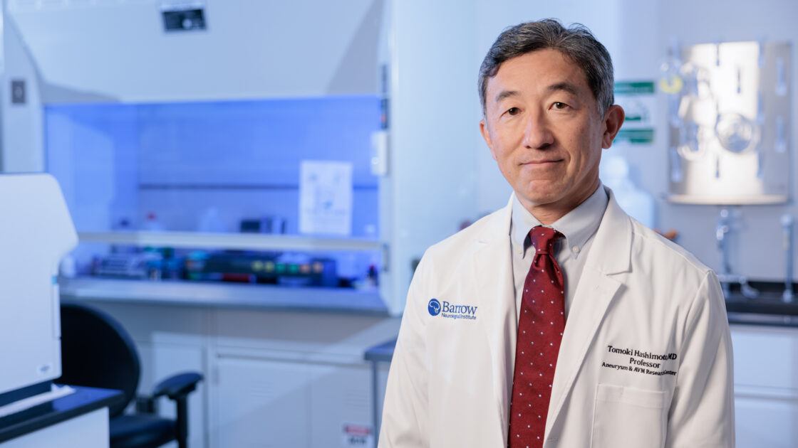 Dr. Tomoki Hashimoto poses in his laboratory in the Barrow Aneurysm and AVM Research Center. He is wearing a white lab coat.