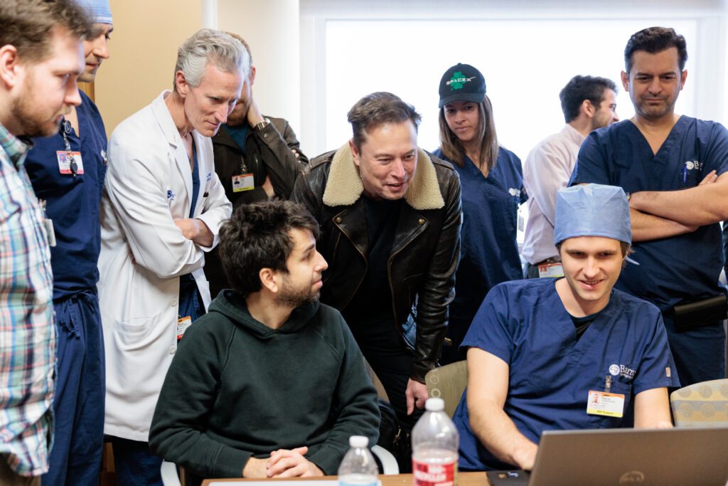 Elon Musk, Dr. Michael T. Lawton, Dr. Francisco Ponce and others gather around a laptop as part of the Neuralink study