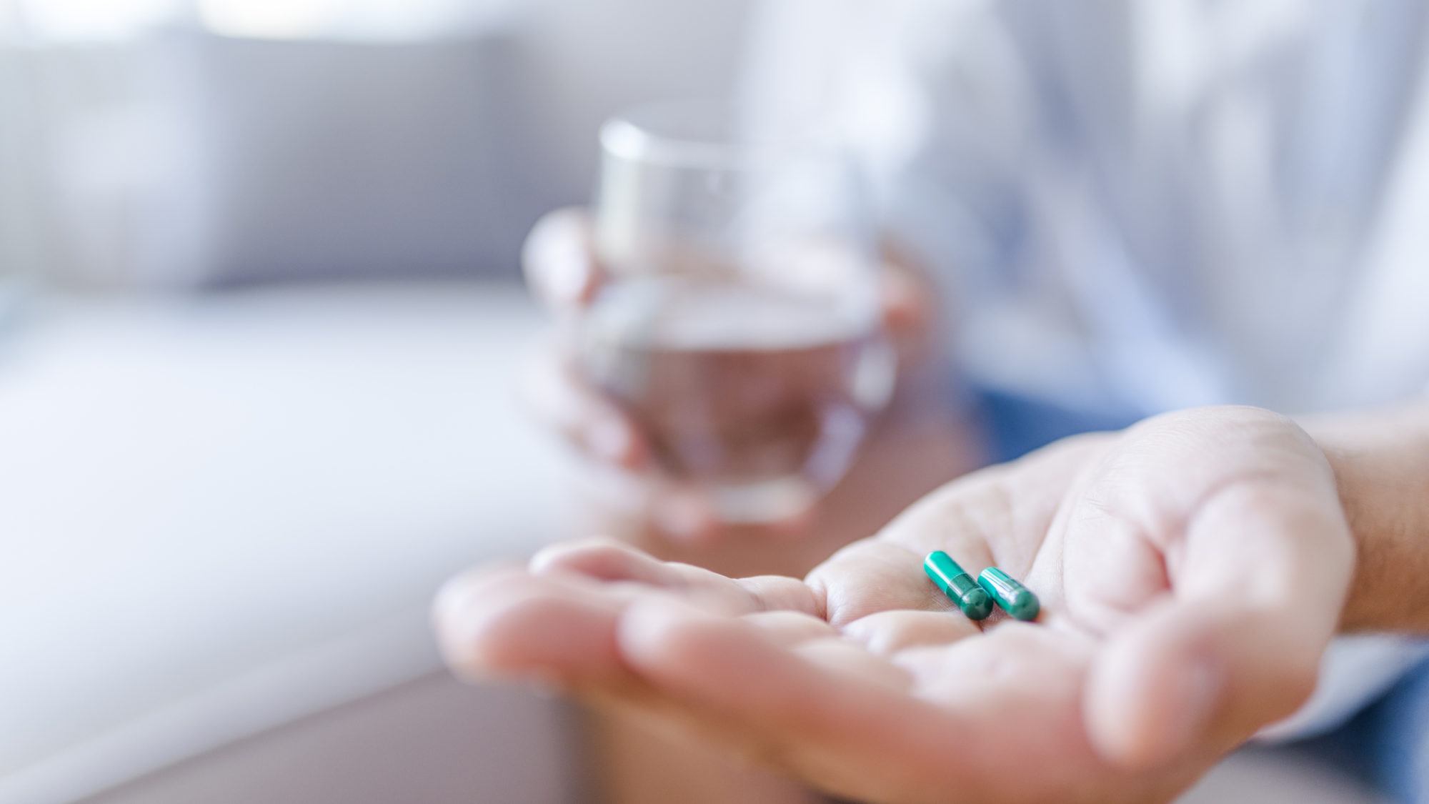 one hand with pills and the other hand holding a glass of water