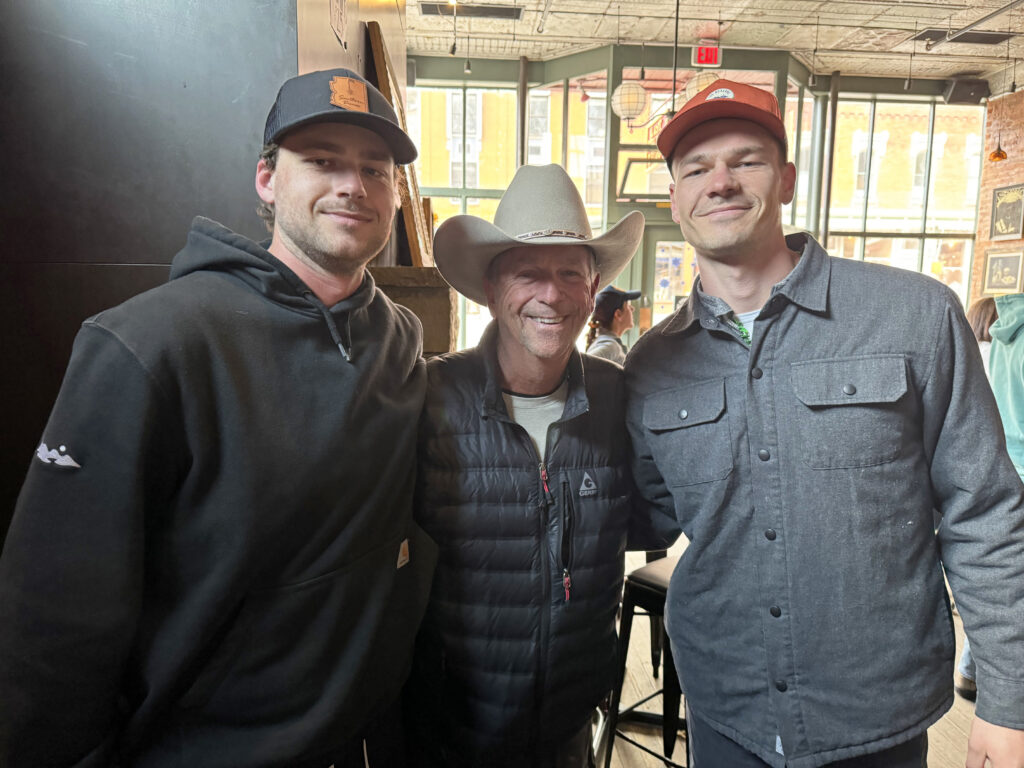 John and his two sons pose for a photo inside a business in Telluride. They are dressed in warm clothing and smiling at the camera.